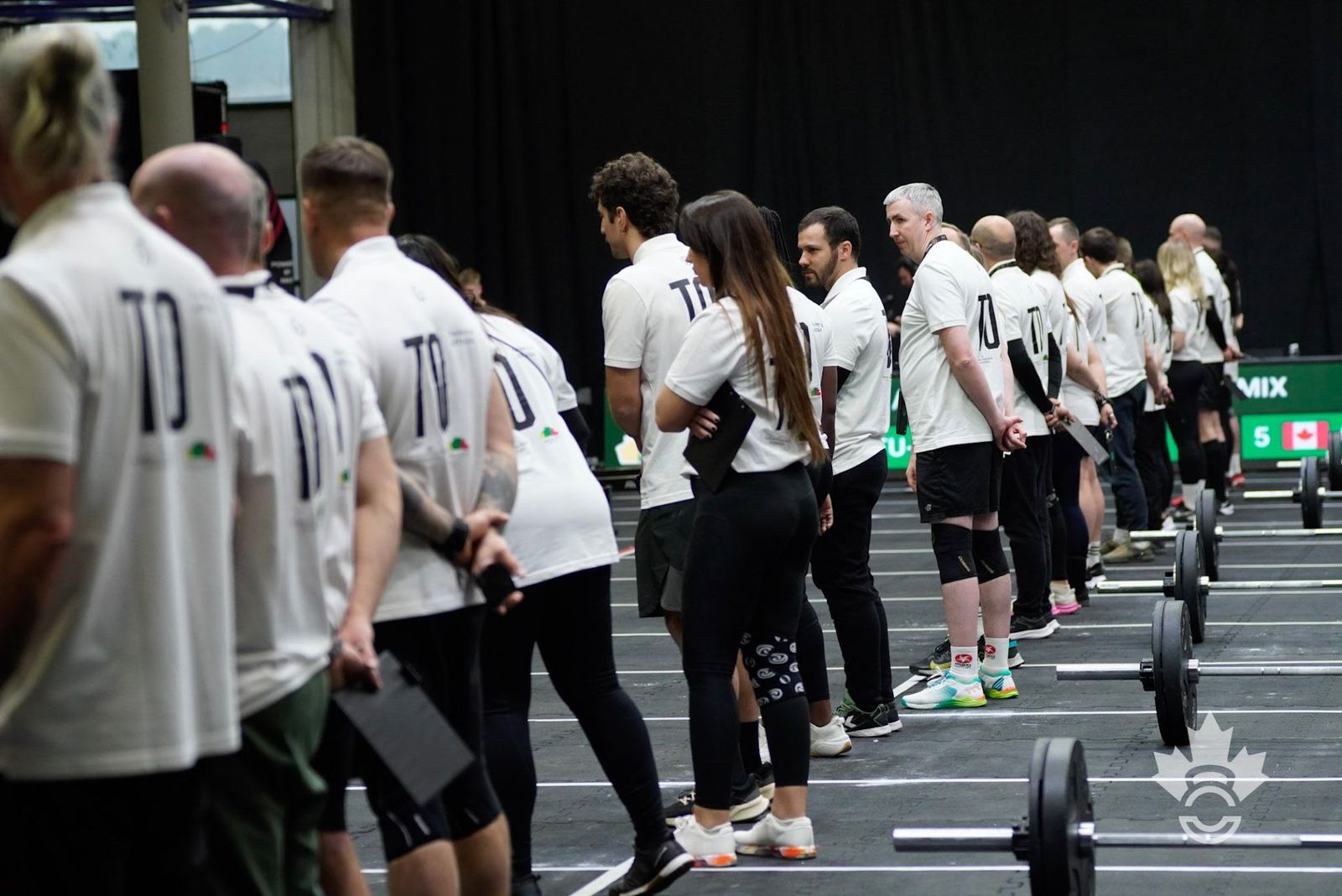A long line of Technical Officials in white TO shirts, clipboards in hand, standing at their lanes before a heat